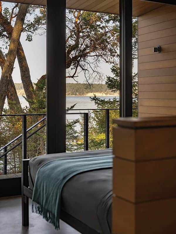 A view of a lake and forest from inside a modern waterfront retreat, seen through floor-to-ceiling windows.