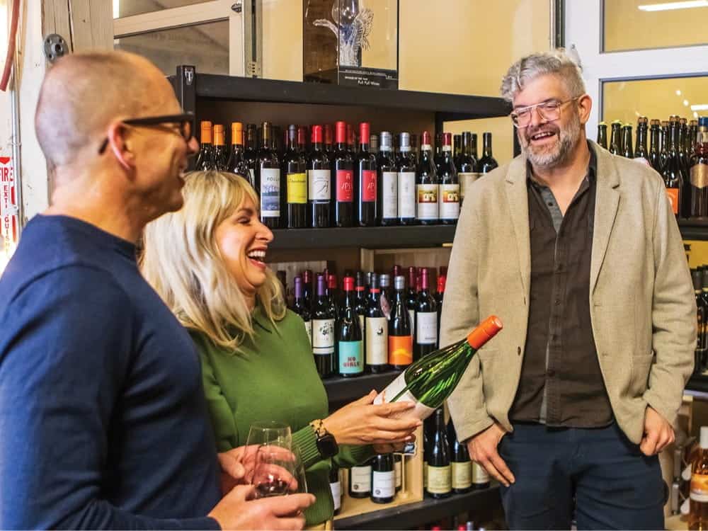 Three people talk and look at a bottle of wine inside the Full Pull Wines store.
