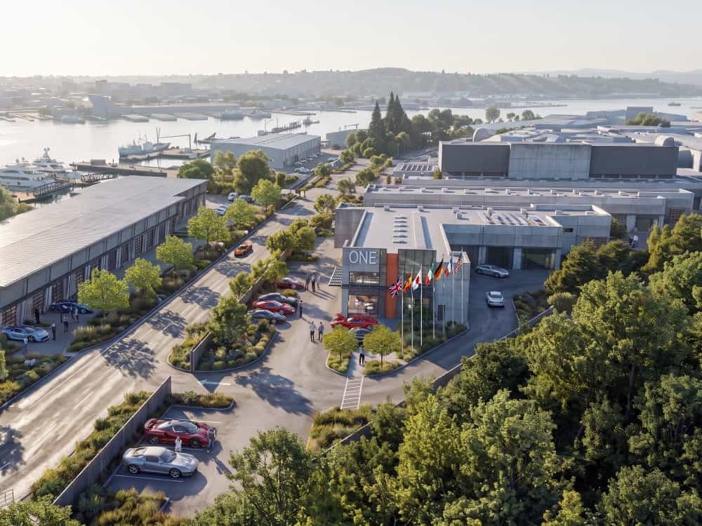 Aerial view of the Terminal One Motor + Yacht Club, featuring a commercial complex labeled “ONE” with sports cars parked in the lot and along the driveway near the harbor.