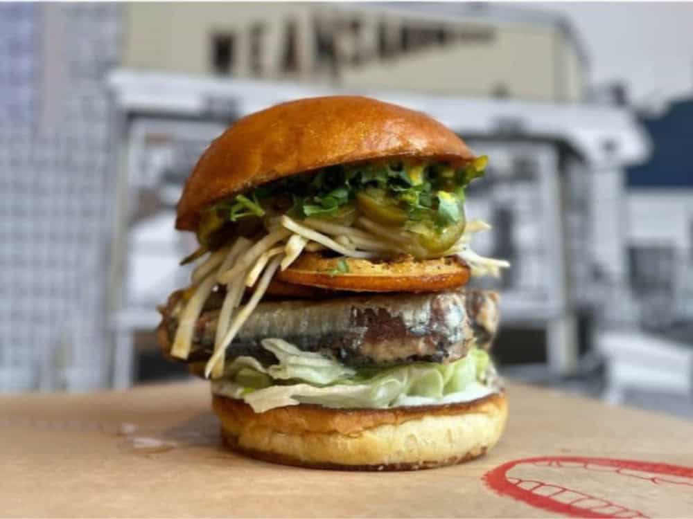 A sardine burger topped with sprouts, greens, and jalapeños on a toasted bun at MEAN Sandwich.