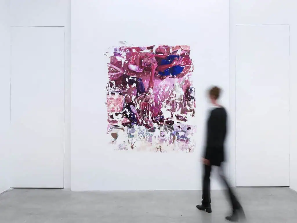 A person walks past an abstract painting with pink and blue brushstrokes hanging on a white gallery wall.