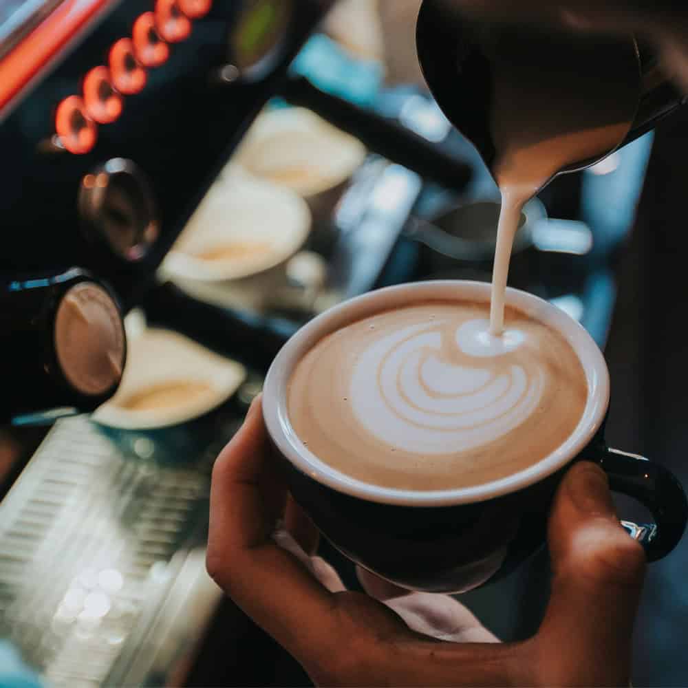Steamed milk being poured into a cup of coffee to create latte art, perfect for a coffee restaurant roundup.