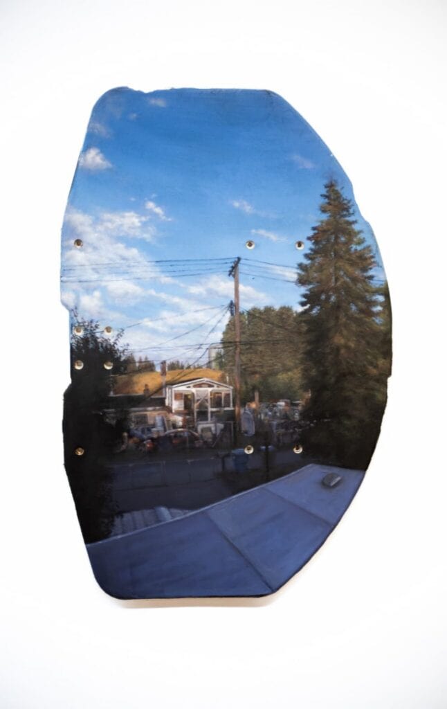 A skateboard deck shaped like a jagged stone, painted with a realistic landscape of a house, power lines, and a tall pine tree under a blue sky.