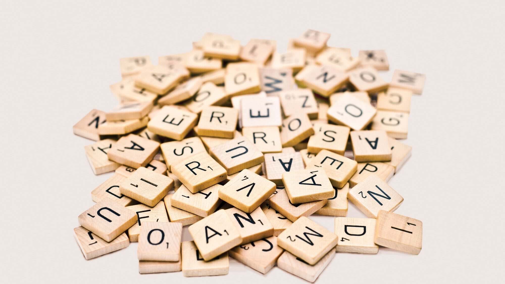 A pile of wooden letter tiles, randomly arranged against a white background, evokes the charm and mystery of the Land Of Enchantment.
