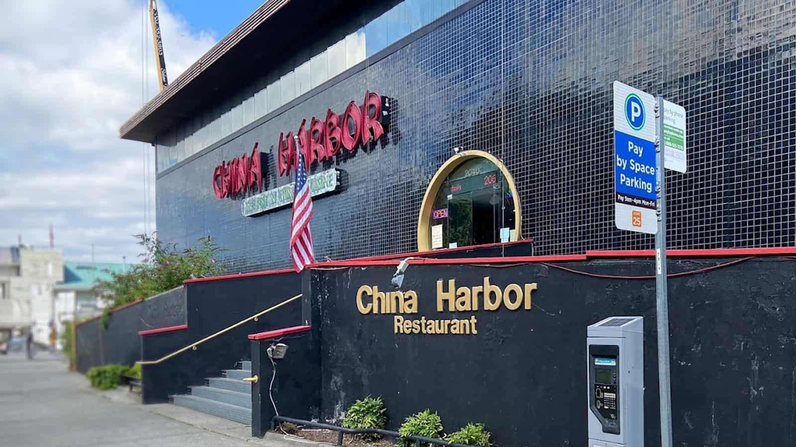 Entrance to the iconic Seattle restaurant, China Harbor, with a "Pay By Space Parking" meter and an American flag displayed outside. The building has a black tile exterior and red signage, making it easy to spot from close by.
