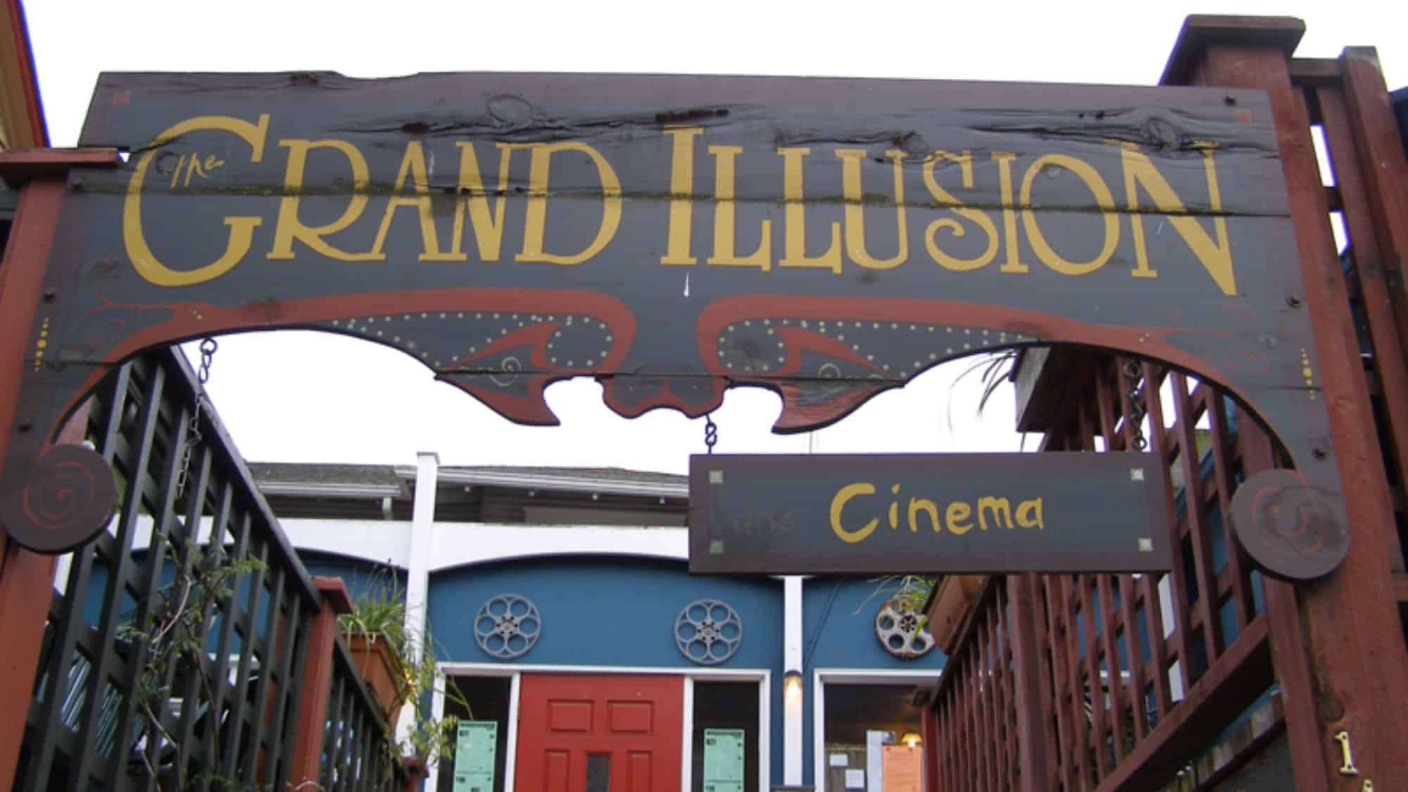Entrance sign for The Grand Illusion Cinema, featuring a moving wooden archway with decorative lettering and a smaller hanging sign that reads "Cinema.
