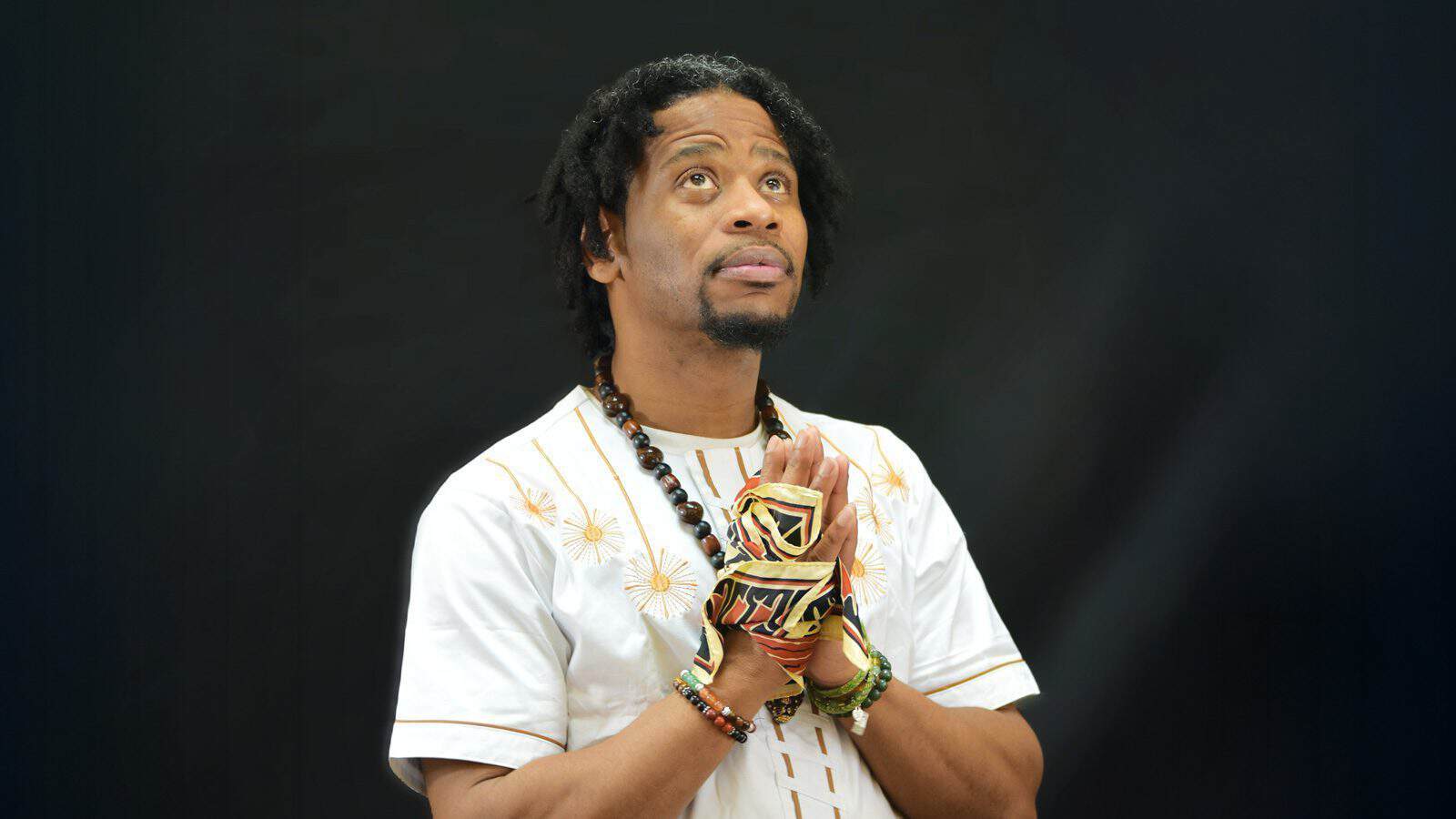 A person wearing a white embroidered shirt and patterned gloves is looking upward into the vast space, seeking a moment of healing against the dark background.