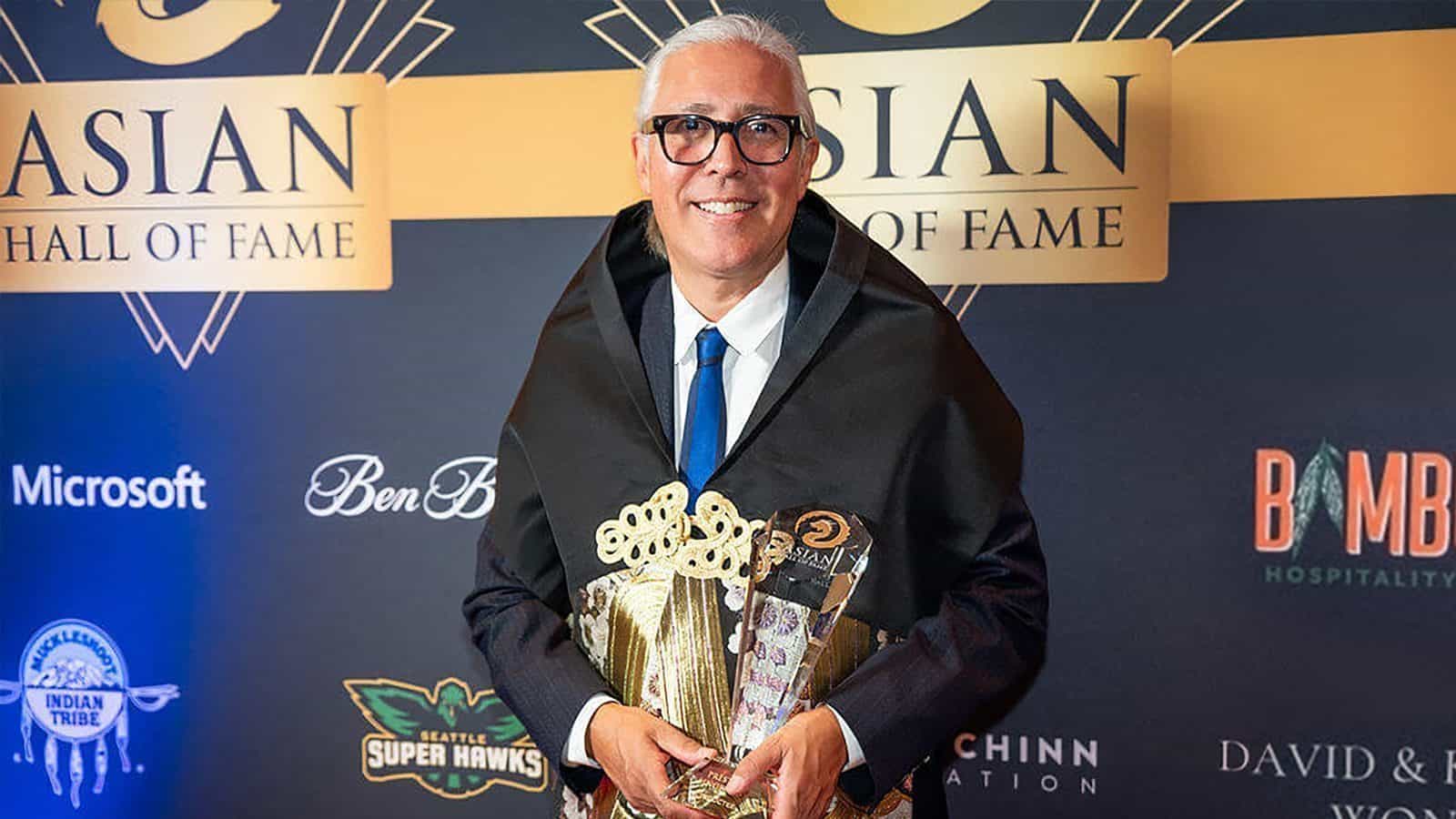 Grinning broadly, Preston Singletary proudly clutches his awards against the "Asian Hall of Fame" backdrop, embodying the spirit of a true Harmonic Alchemist.