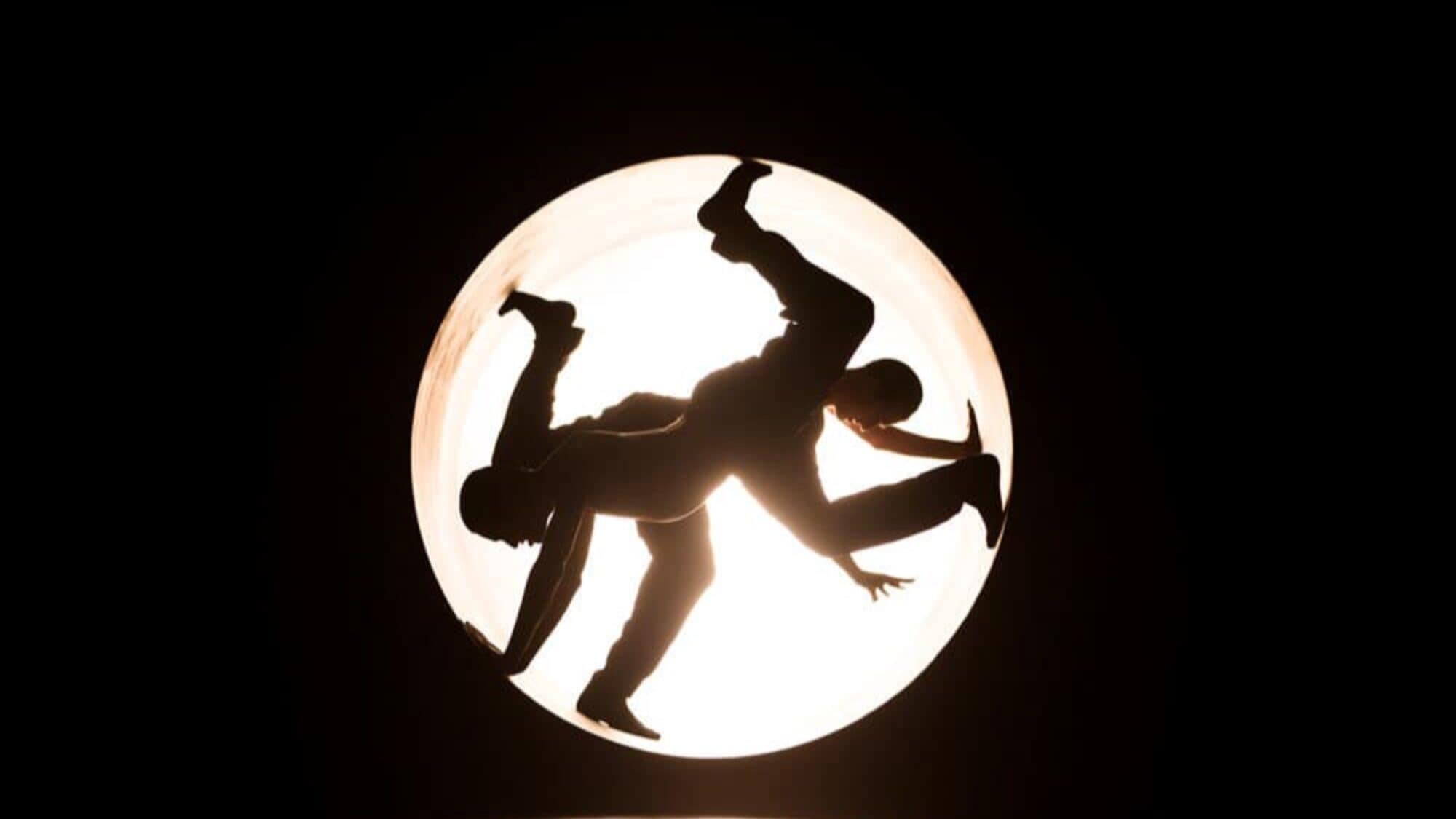 Silhouettes of two people gracefully balancing and performing acrobatic poses inside a lit circular frame against a dark background—a captivating highlight for those exploring what to do in Seattle.