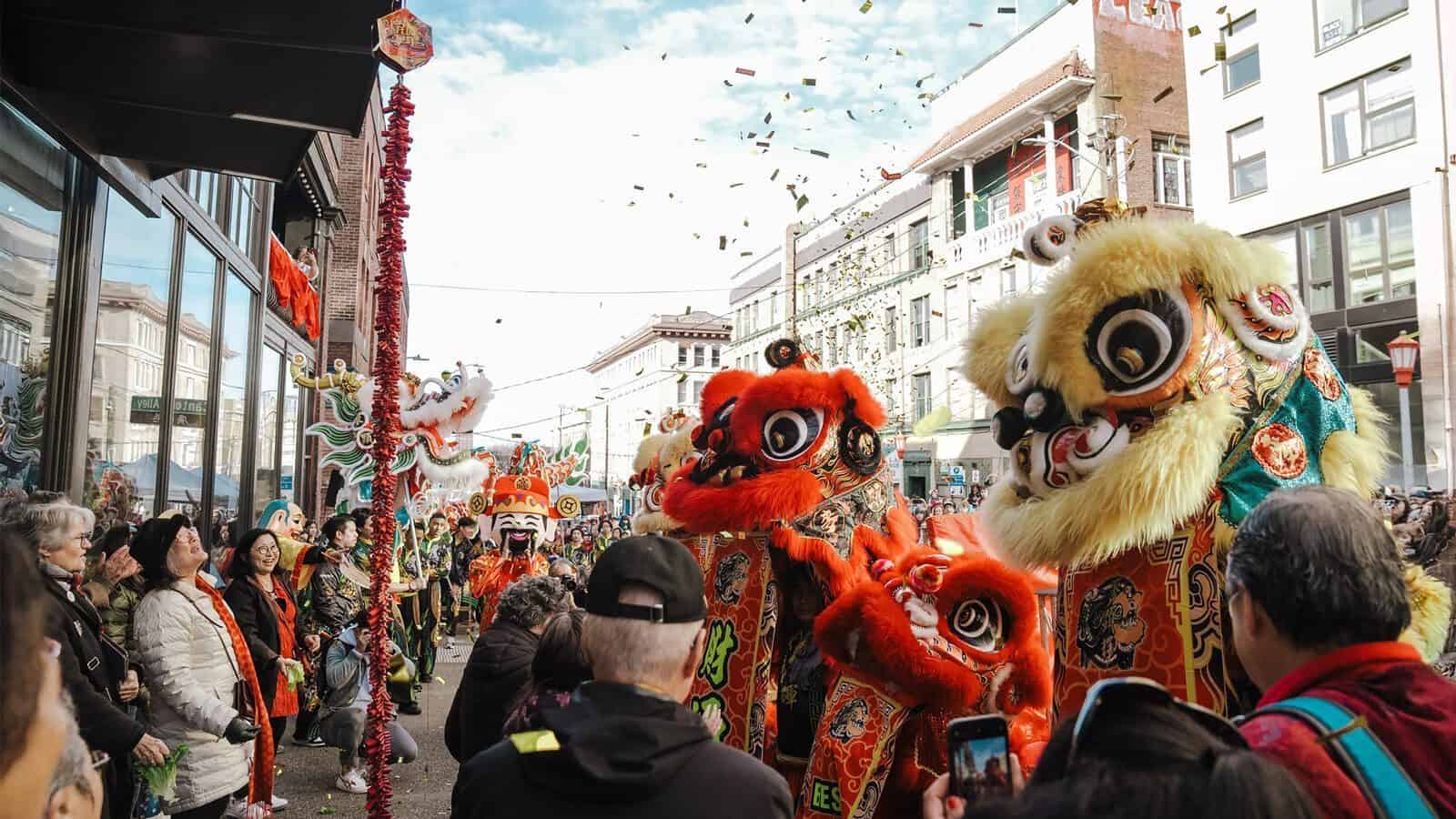 Crowd watches traditional lion dancers perform on a city street during Sound To Summit: AANHPI Voices Rising in Seattle, with confetti in the air and decorated buildings in the background.