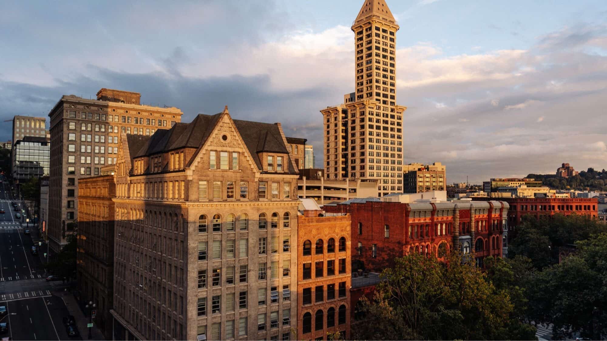 Historic downtown buildings with a mix of architectural styles, including a tall clock tower, under a partly cloudy sky at sunset.