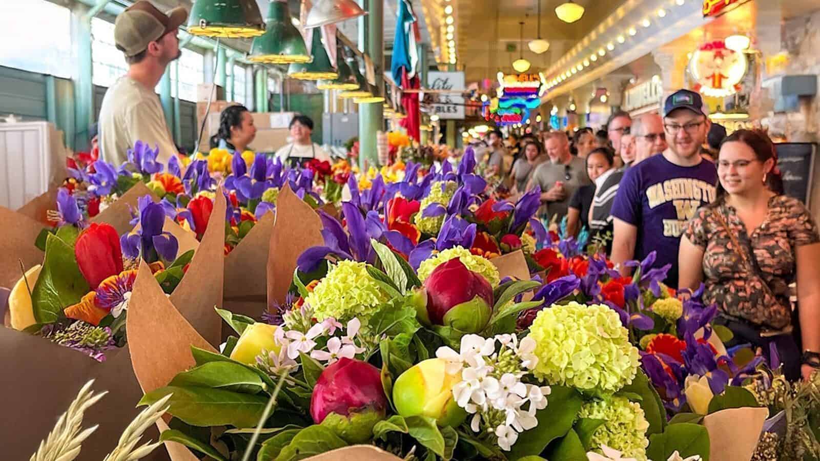 People stand in line at an indoor market in front of vibrant flower bouquets—one of the fun things to do on a weekend, especially with the colorful lights, signs, and perfect blooms for Mother’s Day.