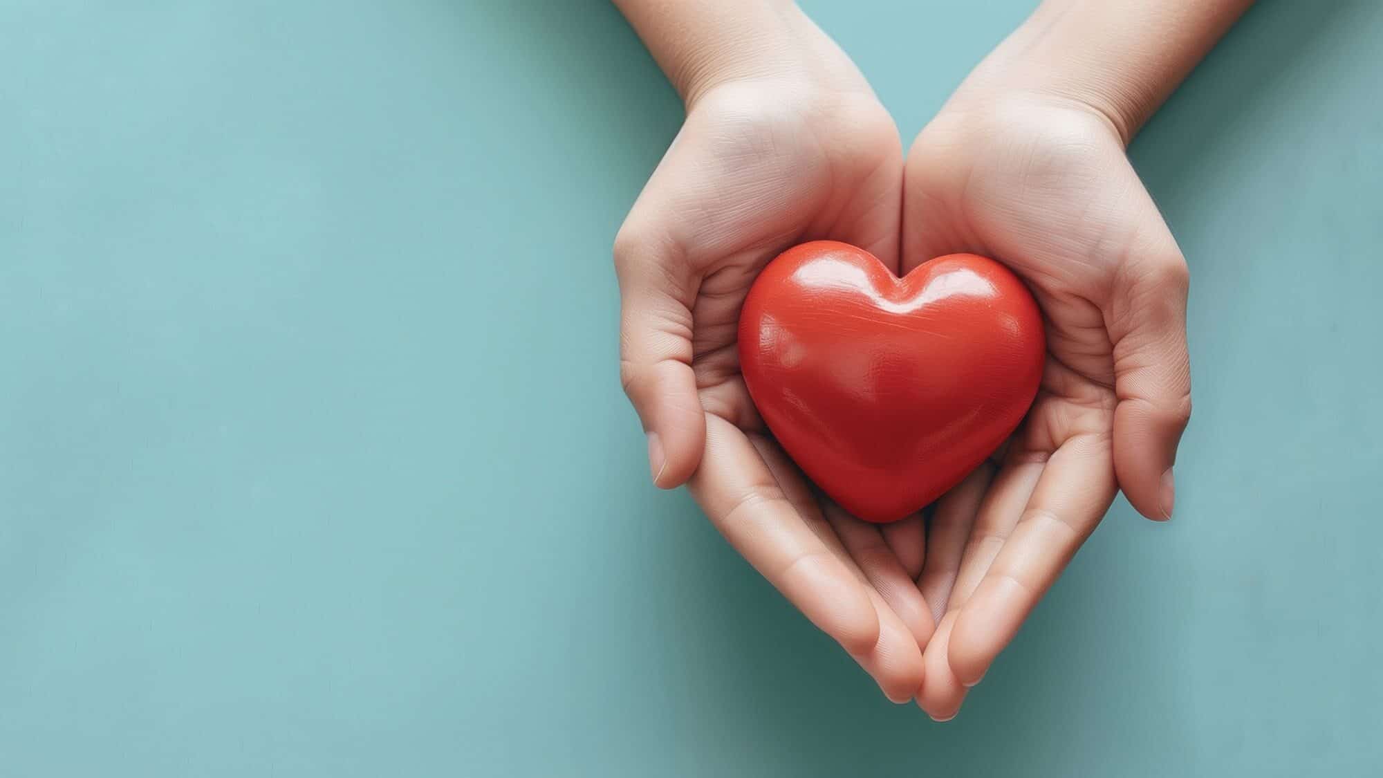Two hands gently cup a smooth, red heart-shaped object against a light blue background, symbolizing better habits for self-care and overall health care.