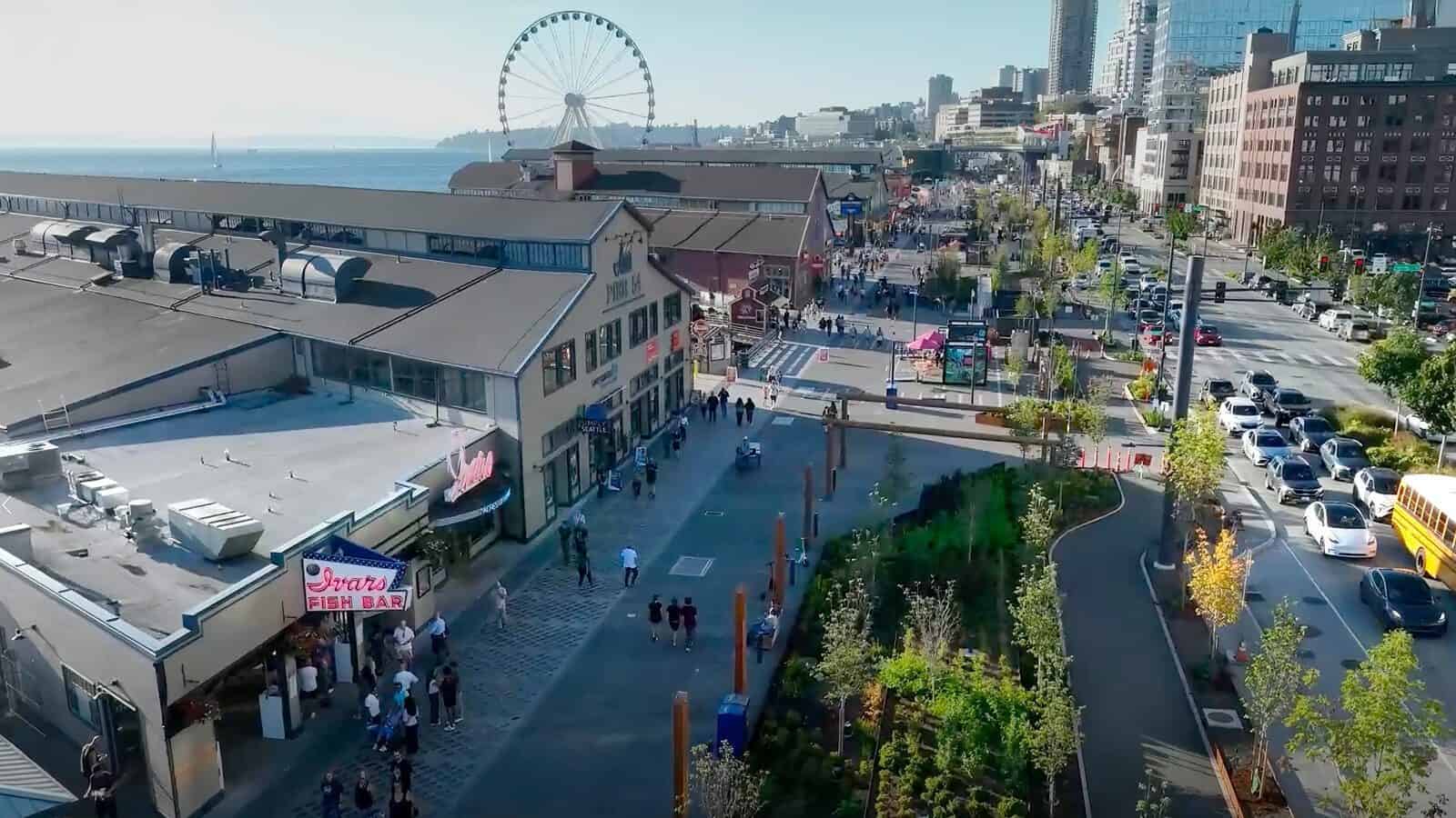 Aerial view of a busy Seattle waterfront area with people walking, green landscaping, a large building, and a Ferris wheel by the water—showcasing this vibrant U.S. walkable city.