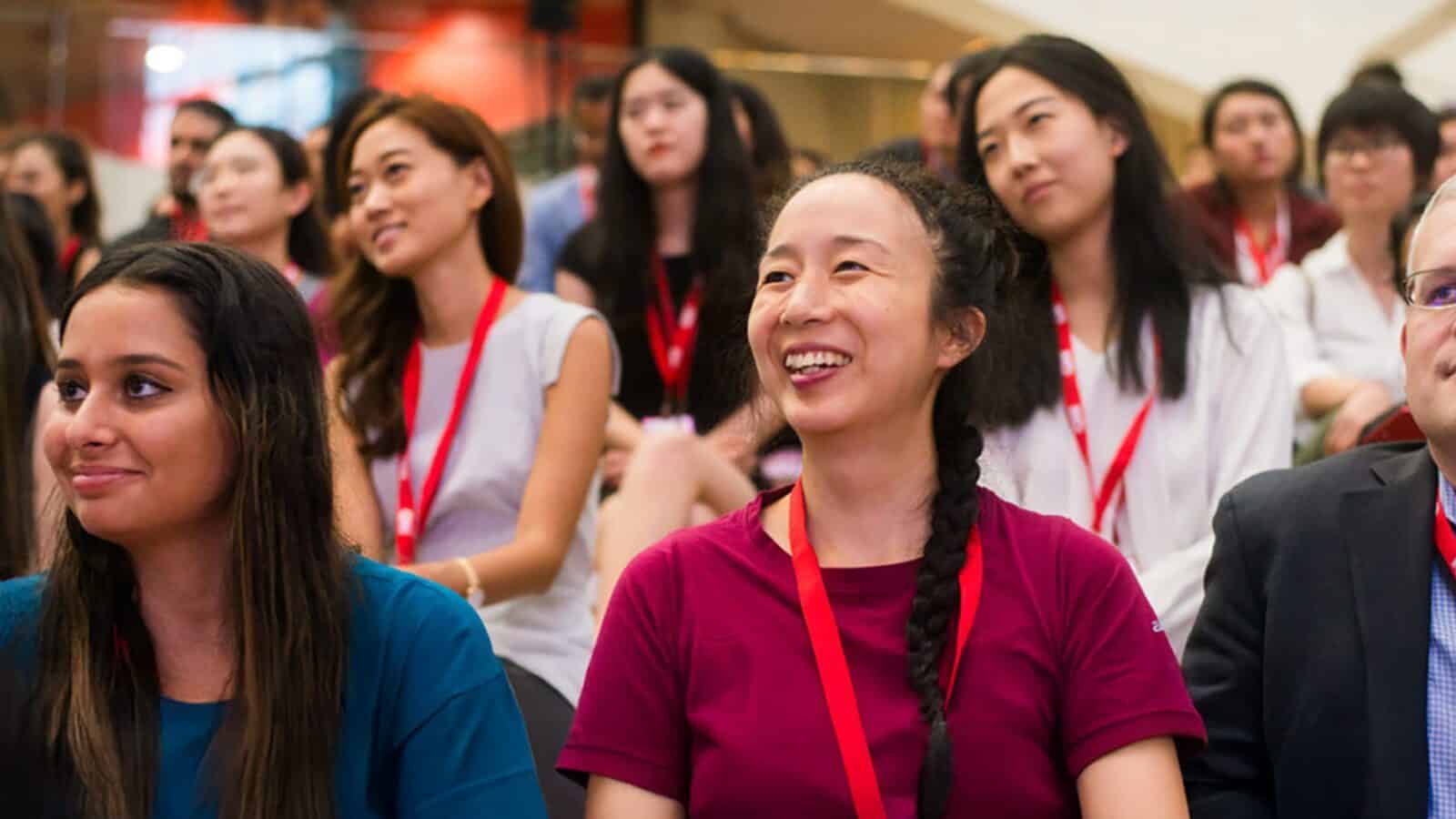 A group of people wearing red lanyards sit together indoors, smiling and listening attentively during an AAJA event or Back to the Future-themed presentation.