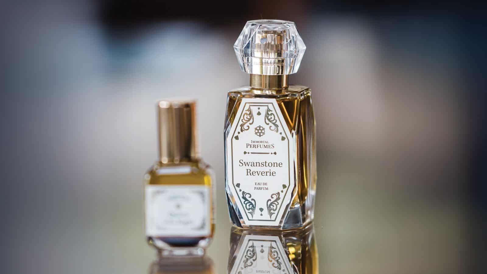 Two glass perfume bottles are displayed: the larger is "Swanstone Reverie" by Jen Siems with a faceted cap, while a smaller, unlabeled perfume with a gold cap sits beside it.
