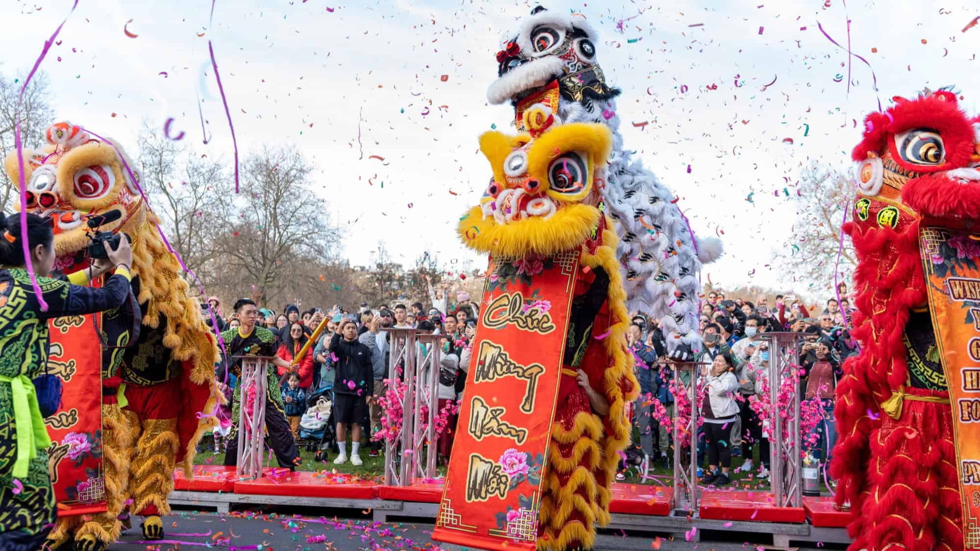 Performers in lion costumes celebrate with banners and confetti at a vibrant cultural festival, with a crowd of people watching in the background—a lively scene reminiscent of Seattle Center Festál events.