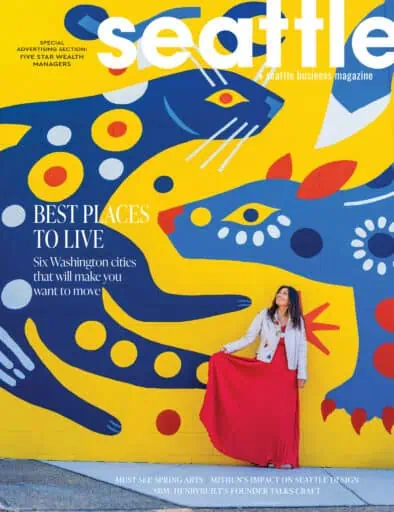 A woman in a red skirt stands in front of a colorful mural featuring large abstract animal shapes on the cover of Seattle Business Magazine.