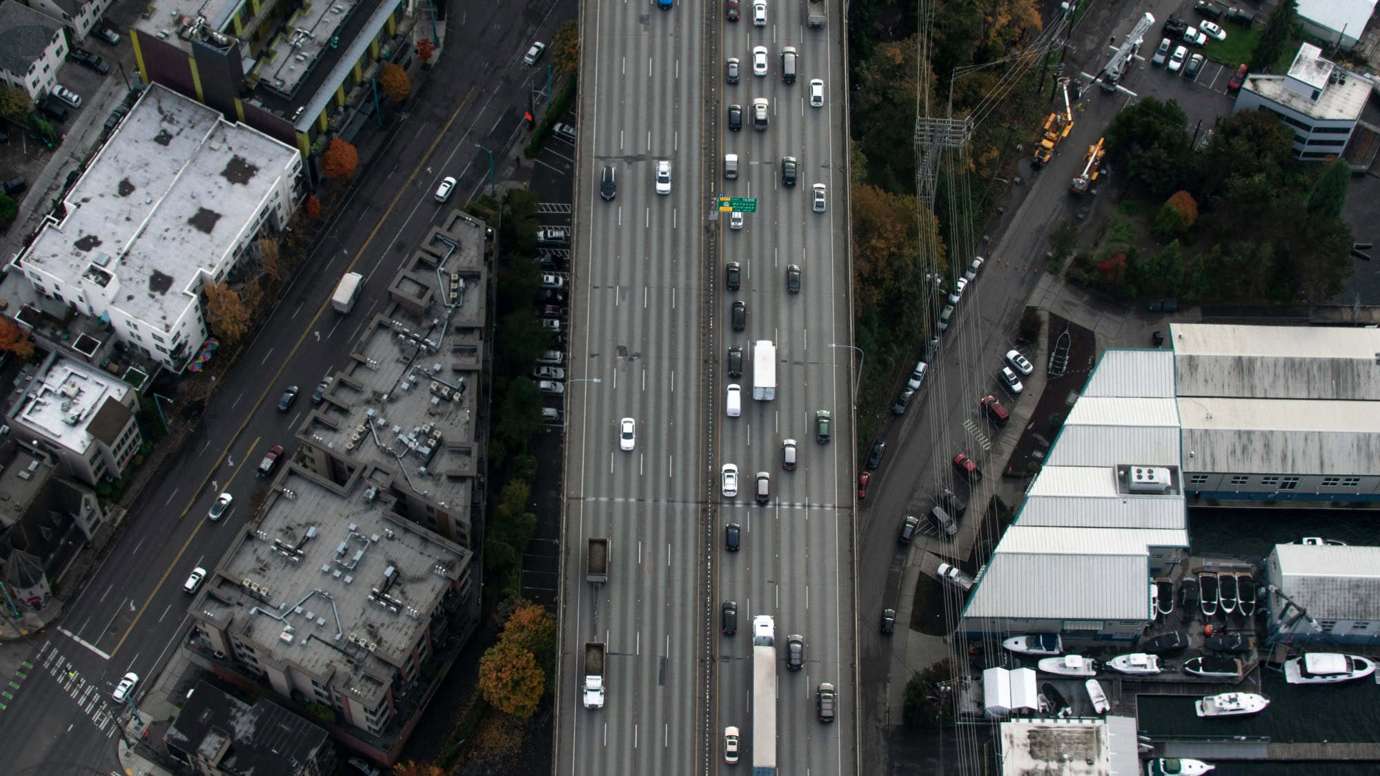 Aerial view of a multi-lane highway with vehicles traveling in both directions, flanked by buildings and parked cars on either side.