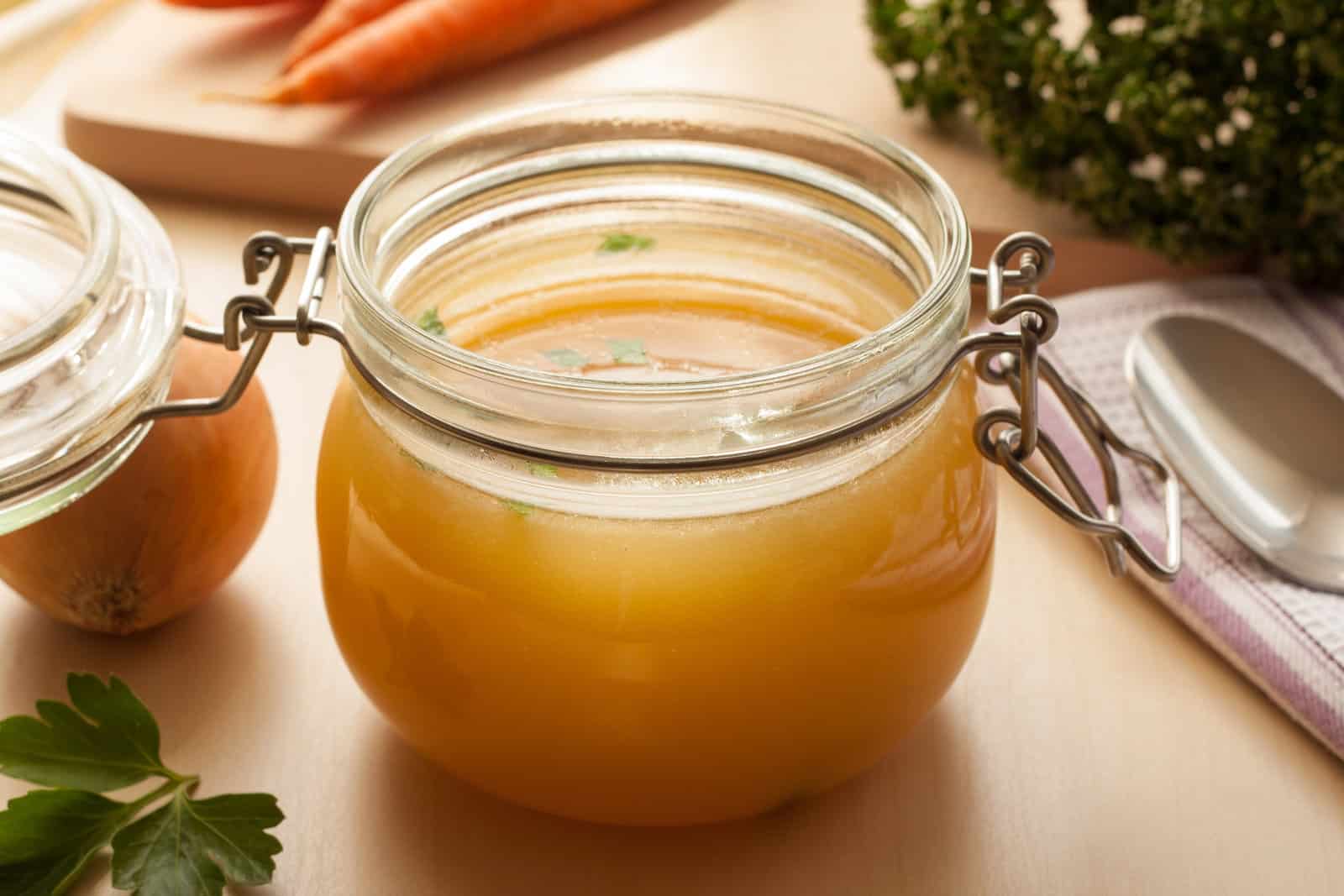 bone-broth-made-from-chicken-in-a-glass-jar-with-carrots-onions-and-celery-root-in-the-background