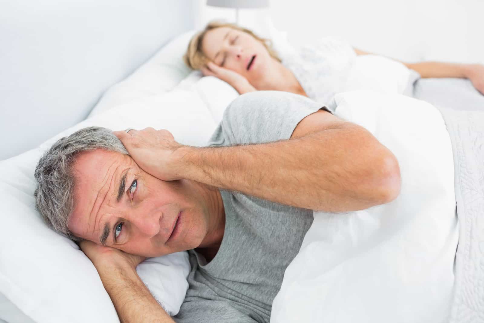 fed-up-man-blocking-his-ears-from-noise-of-wife-snoring-at-home-in-bedroom