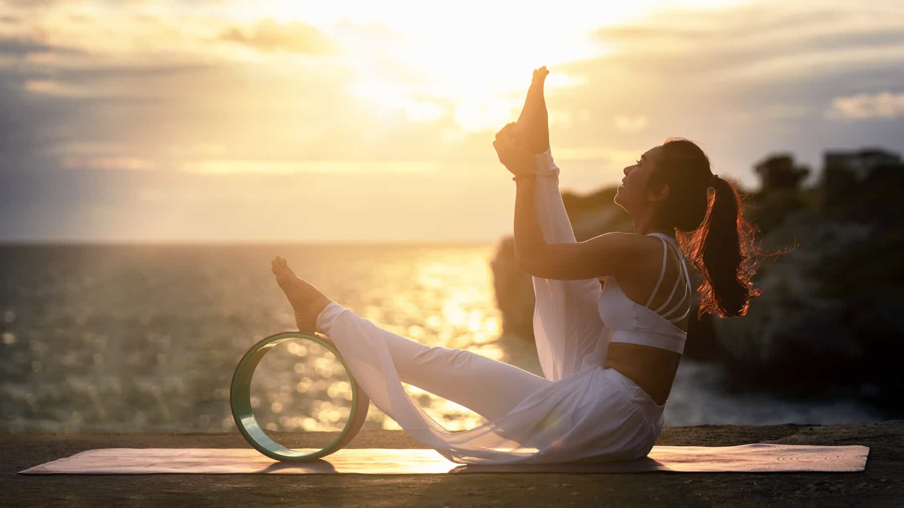 young-woman-exercise-yoga-in-nature-sea-sunset-view-modified-yoga-poses-with-yoga-wheel-stretching-strengthening-exercises-with-advanced-yoga-relaxation-health-care-concept