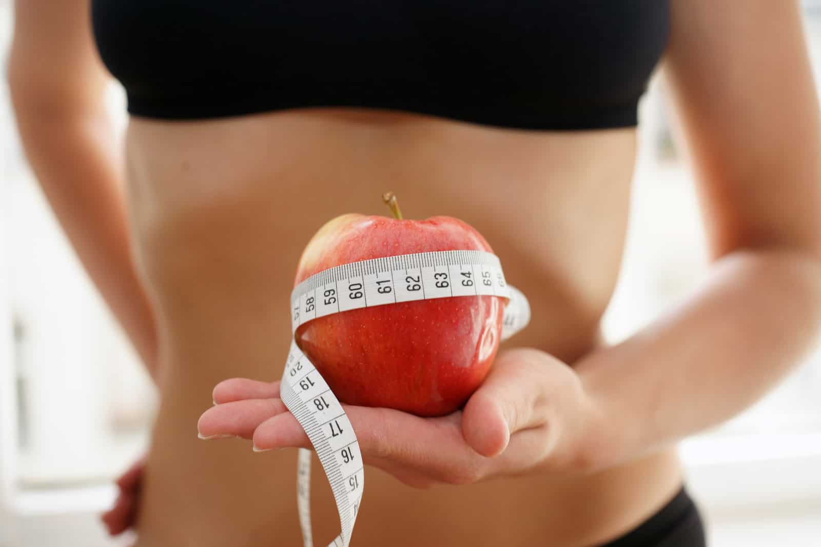 young-slim-woman-in-sports-outfit-holds-apple-with-measure-tape-nutrition-diet