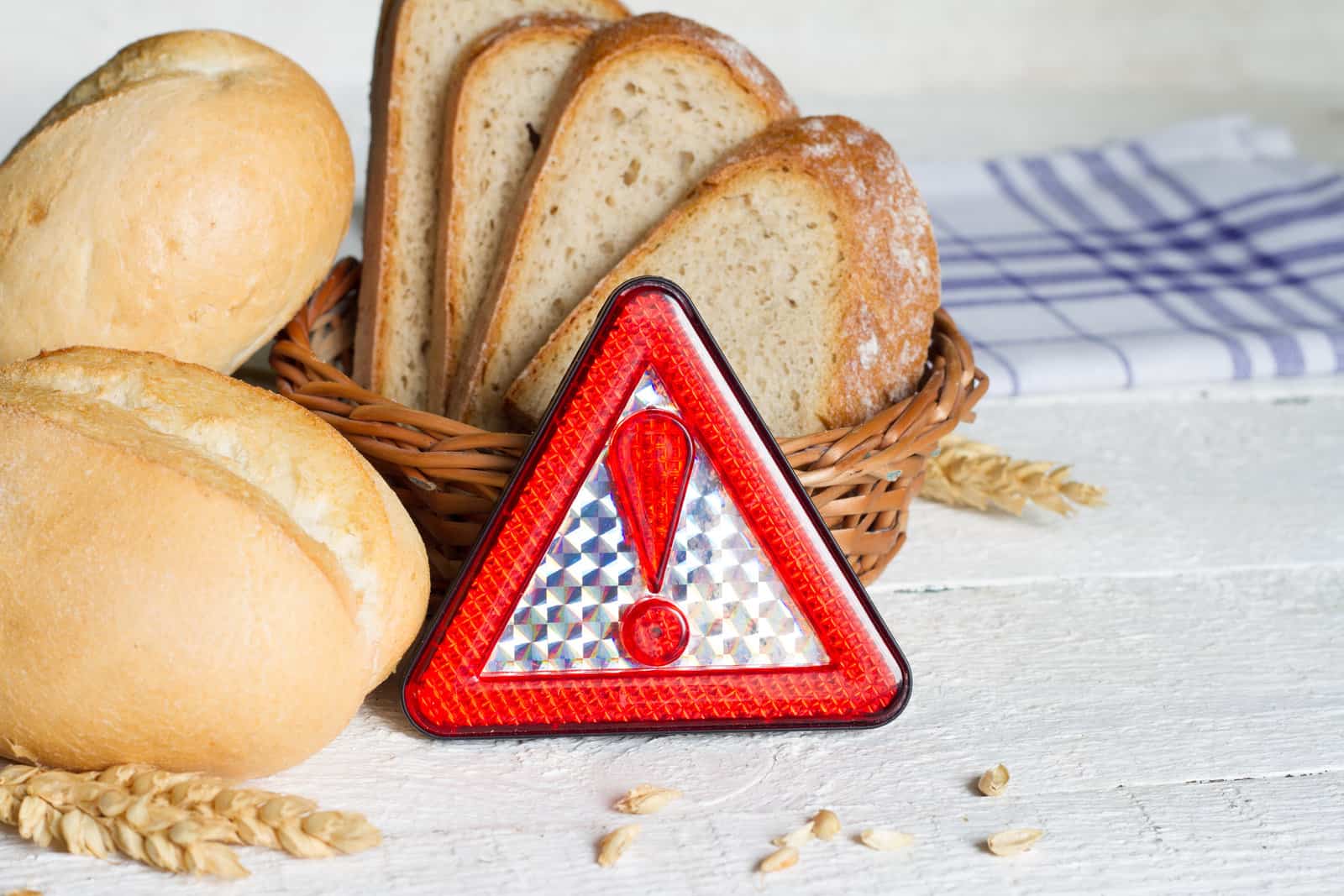 gluten-intolerance-with-bread-wheat-and-warning-sign-on-white-planks-closeup