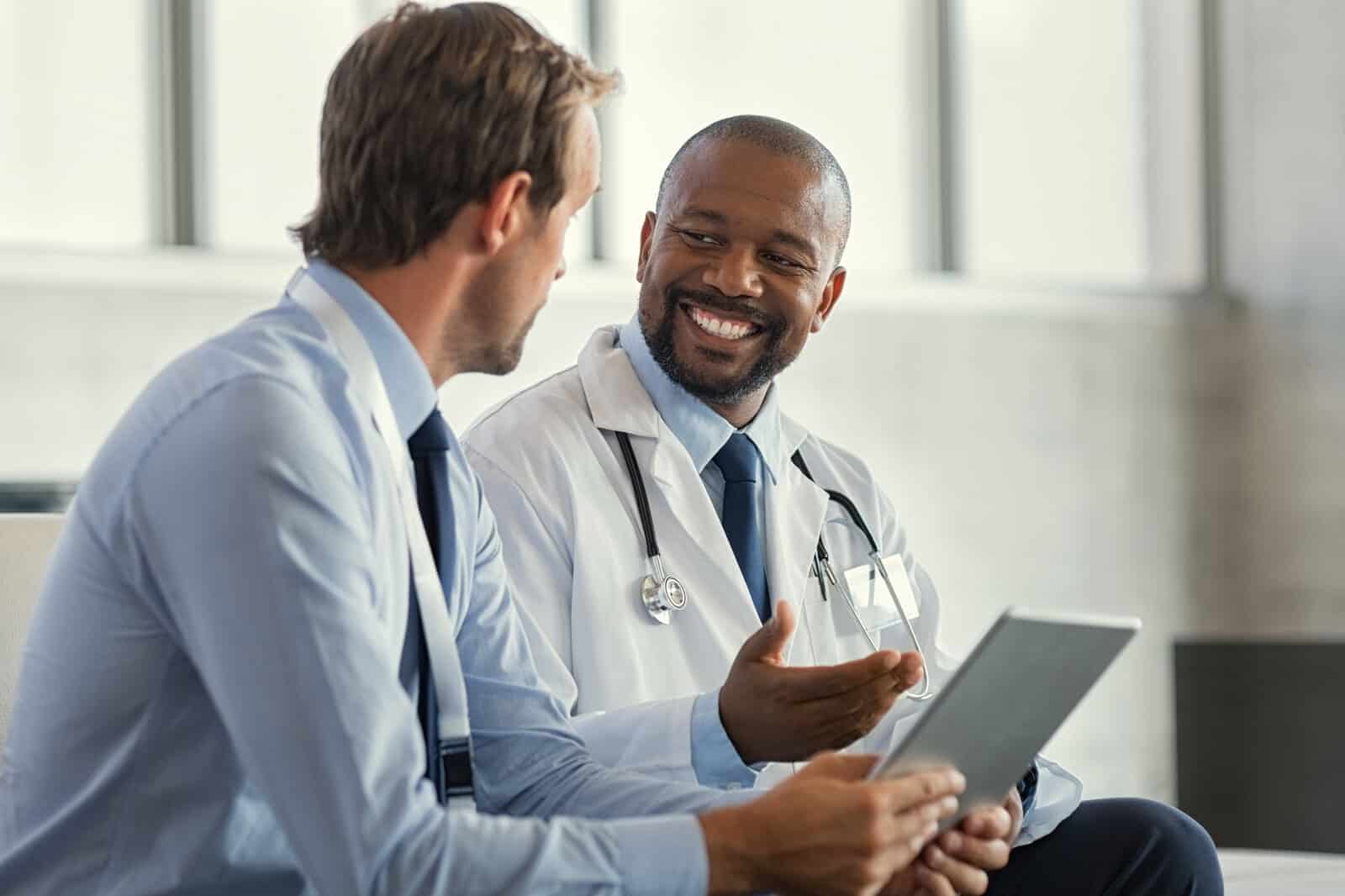 two-mature-smiling-doctors-having-discussion-about-patient-diagnosis-holding-digital-tablet-successful-african-surgeon-discussing-case-after-positive-result-representative-pharmaceutical-discussing