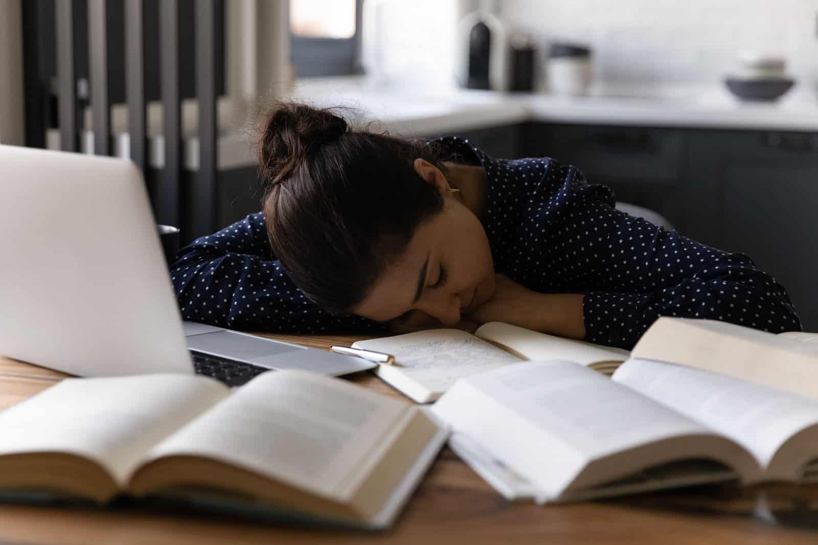 exhausted-tired-indian-graduate-student-girl-sleeping-at-workplace-on-chair-placing-head-down-on-desk-with-laptop-and-open-books-suffering-from-lack-of-sleep-feeling-fatigue-and-overworked