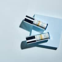 Even Up by Colorescience Pigment Perfector bottles on high contrast turquoise background - available in Canada