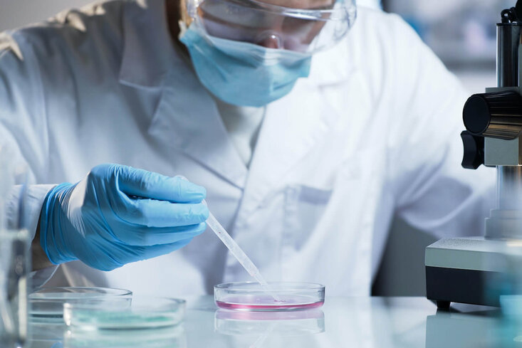 Chemist using an eye dropper tool in a petri dish in a lab depicting skin care product formulation and testing
