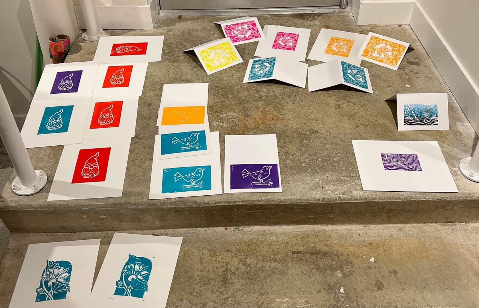 Photo of the many ink prints on white cardstock drying on the concrete steps of the art studio