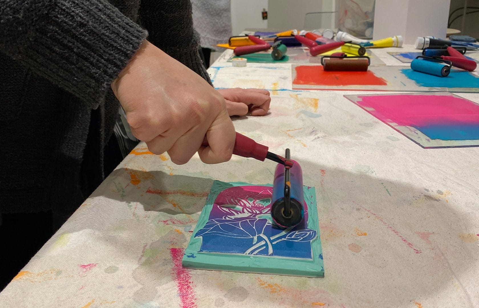 Photo of a hand rolling an ombre pink and blue ink onto a lino block for printmaking