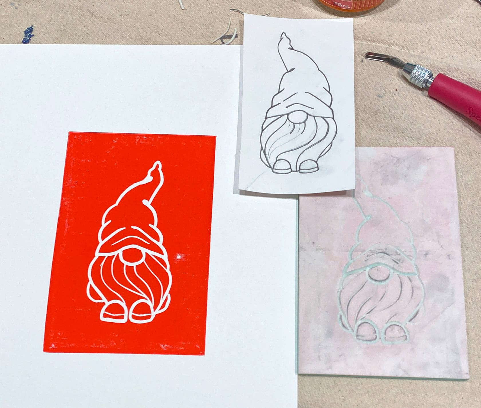 Photo from left to right: red ink print of a gnome, pencil drawn gnome, and a block cut gnome showing process of printmaking