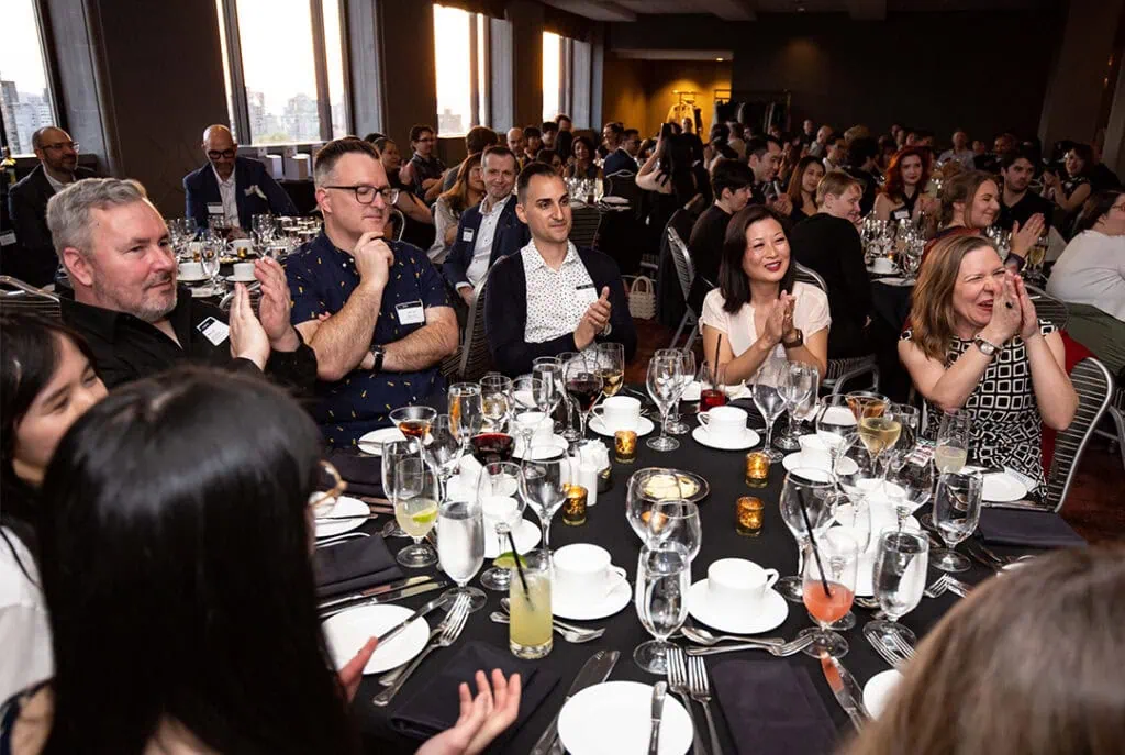 Group photo of several dining tables with people clapping
