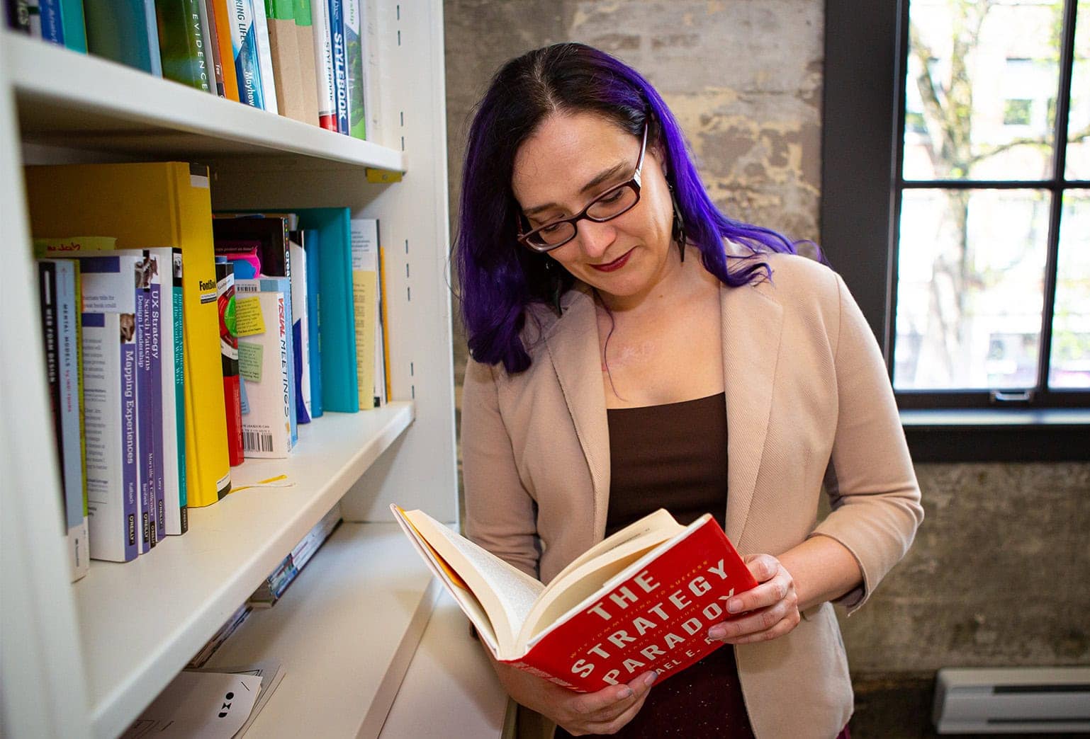 Person standing beside a bookshelf reading a book