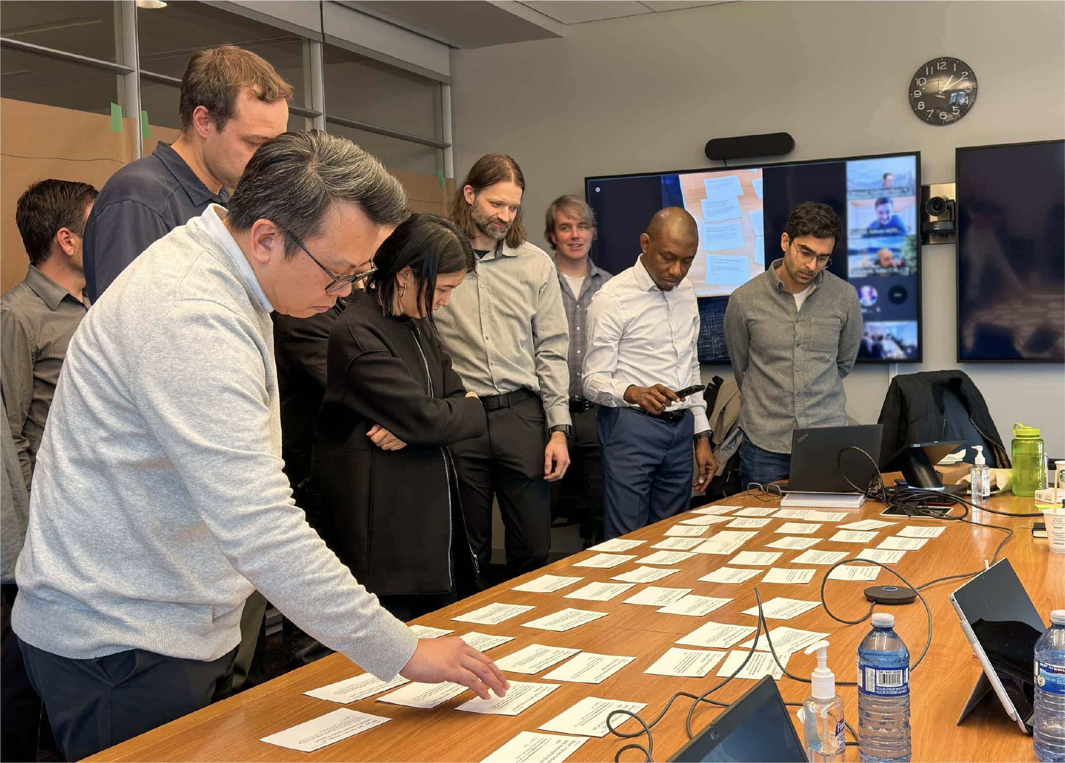 OXD and DriveBC team members organizing cards on a conference table with remote participants on a screen.