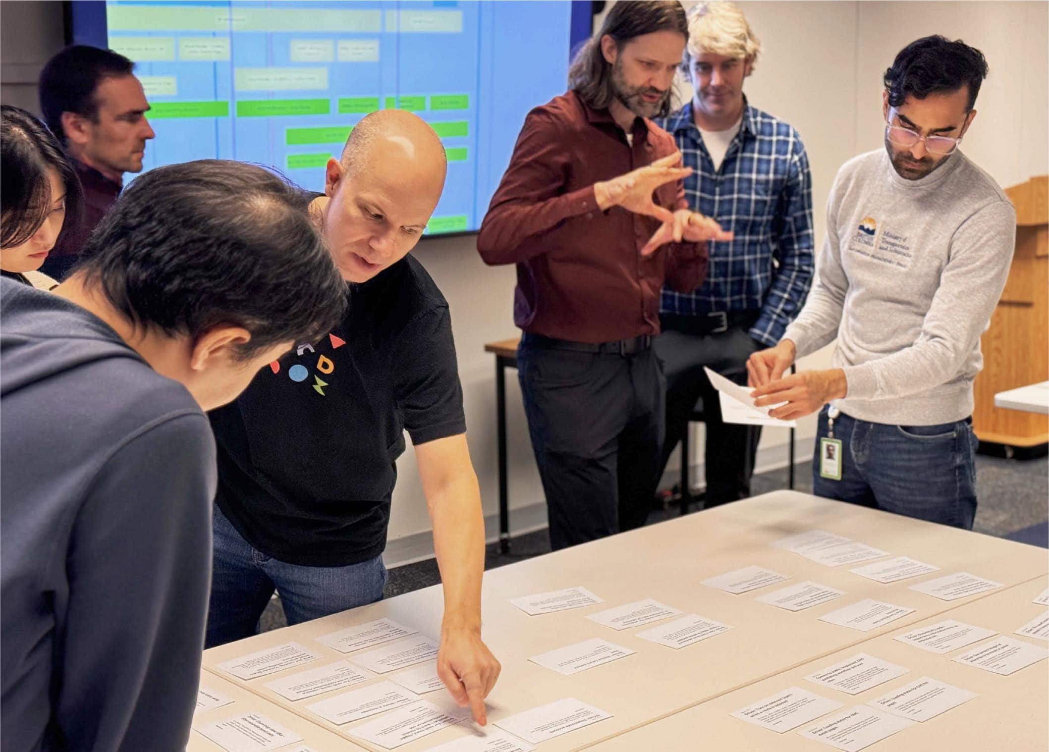 OXD and DriveBC team members sorting index cards on a table during a workshop.
