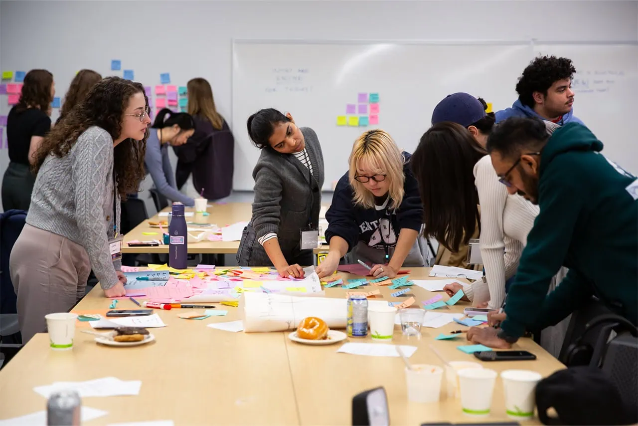 A group of attendees gathered around a table, actively brainstorming and writing on a large spread of colourful sticky notes.
