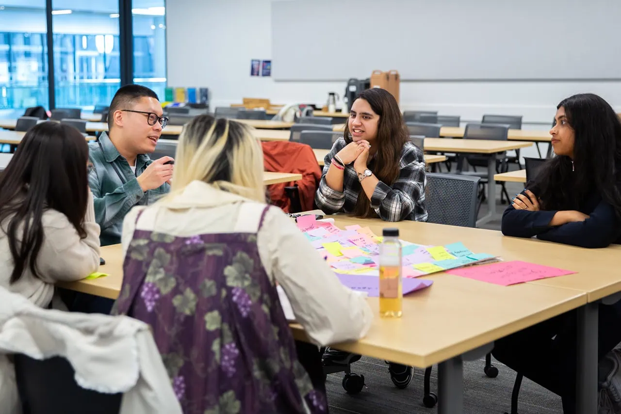 Four participants seated at a table, engaged in a focused group discussion over a spread of sticky notes.