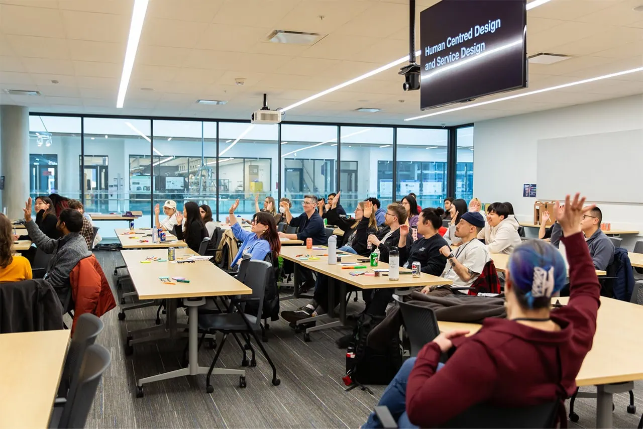 A wide shot of an engaged audience at Vancouver Service Jam raising their hands during a presentation.